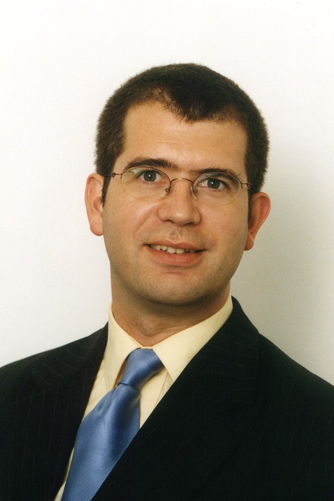 The End of the Beginning. European-male-mid-thirties-smiling-face-head-and-shoulders-formal-business-portrait-dark-pinstripe-suit-yellow-shirt-blue-striped-silk-tie-red-rimmed-lightweight-glasses-1-DHD