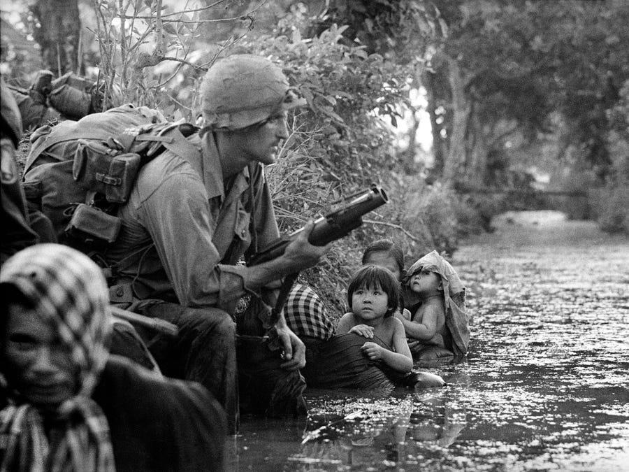 Les Images de la Guerre du Vietnam - Page 3 Two-south-vietnamese-children-gaze-at-an-american-paratrooper-holding-a-grenade-launcher-as-they-cling-to-their-mothers-who-huddle-against-a-canal-bank-for-protection-from-viet-cong-sniper-fire-in-the-bao-trai-area-vietnam