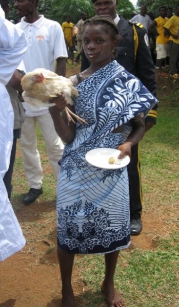 Liberian girl dressed in tranditional cloth with a white chicken, rice and a kola nut to welcome President Sirleaf